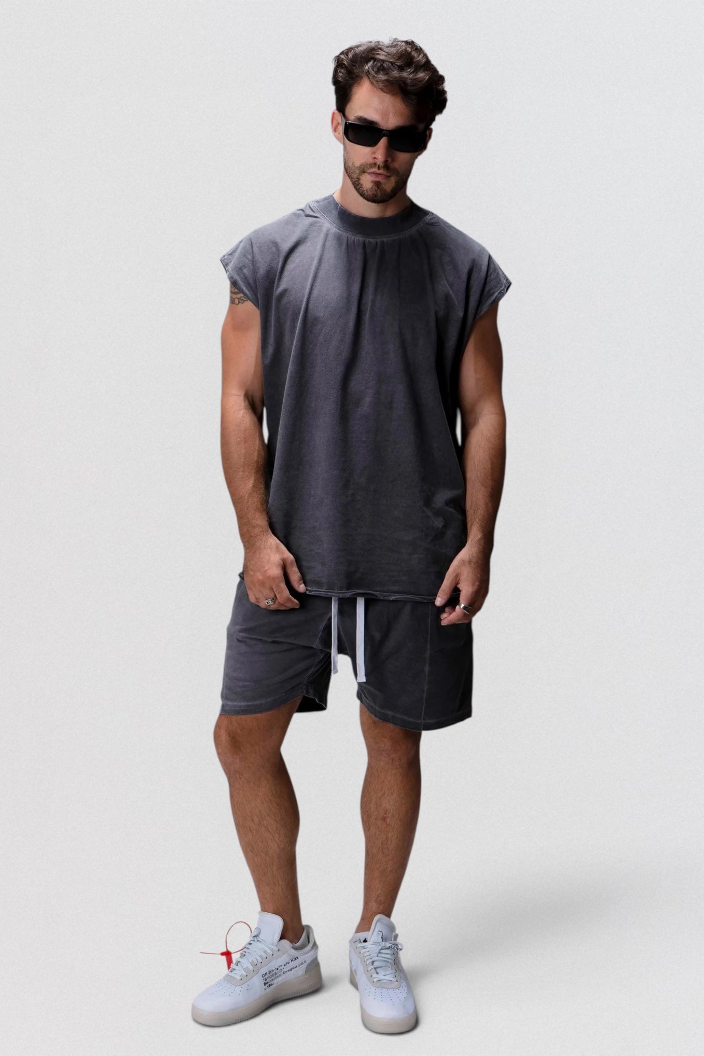 Man wearing a gray sleeveless shirt and shorts on a white background