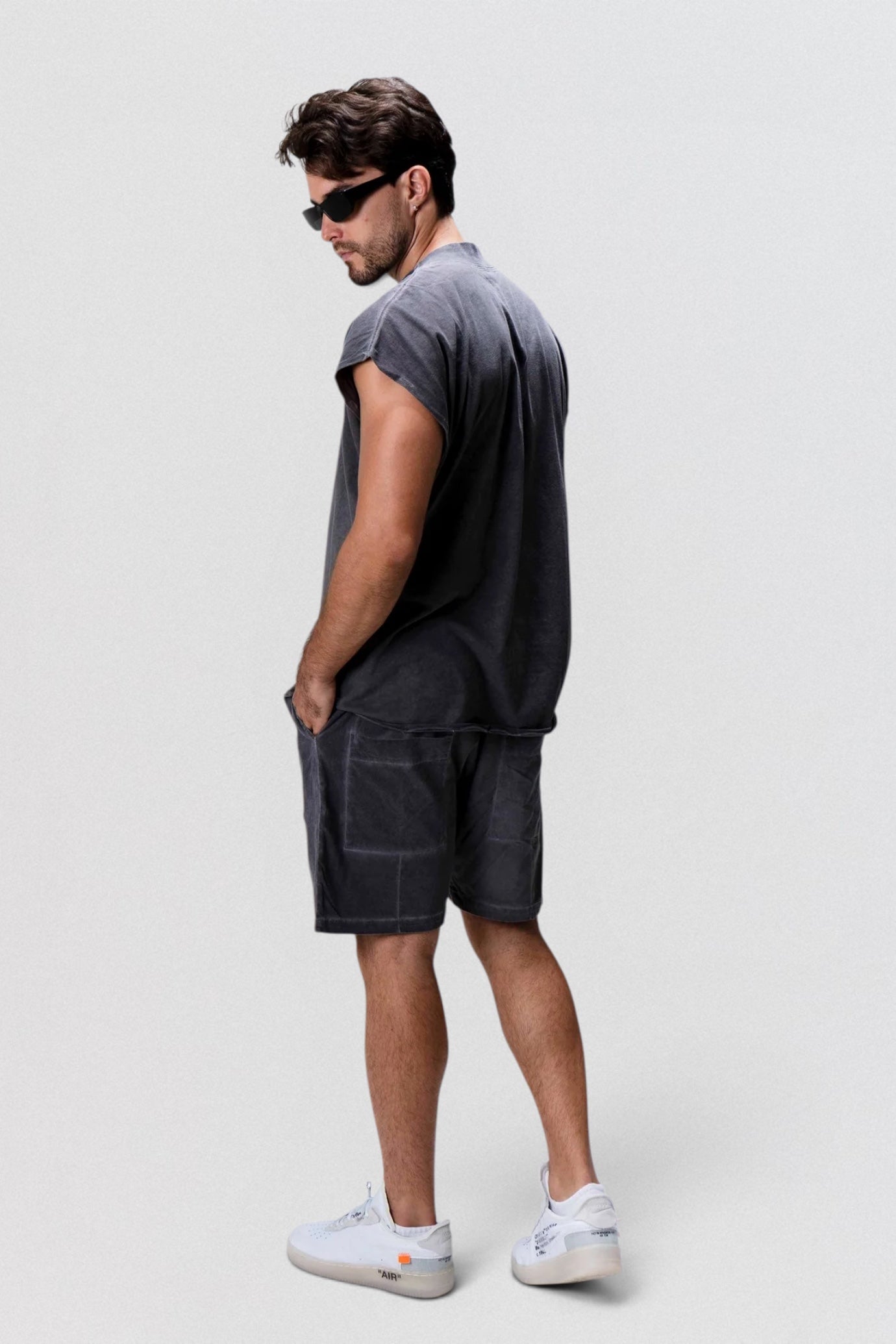 Man wearing a gray t-shirt and dark shorts on a white background