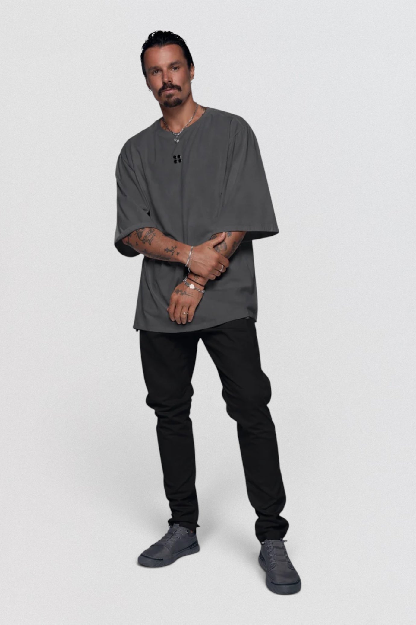 Man wearing a gray oversized t-shirt and black pants on a white background