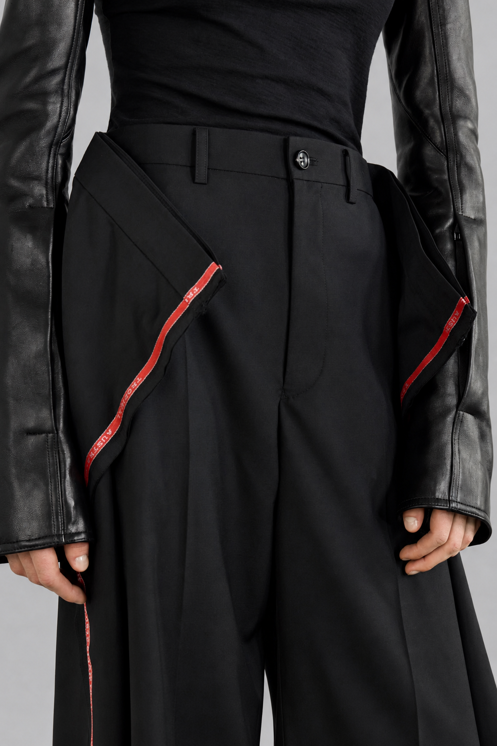 Junya Watanabe SS26 Side Stripes Trousers. Person wearing a black outfit with red accents and a leather jacket on a gray background 