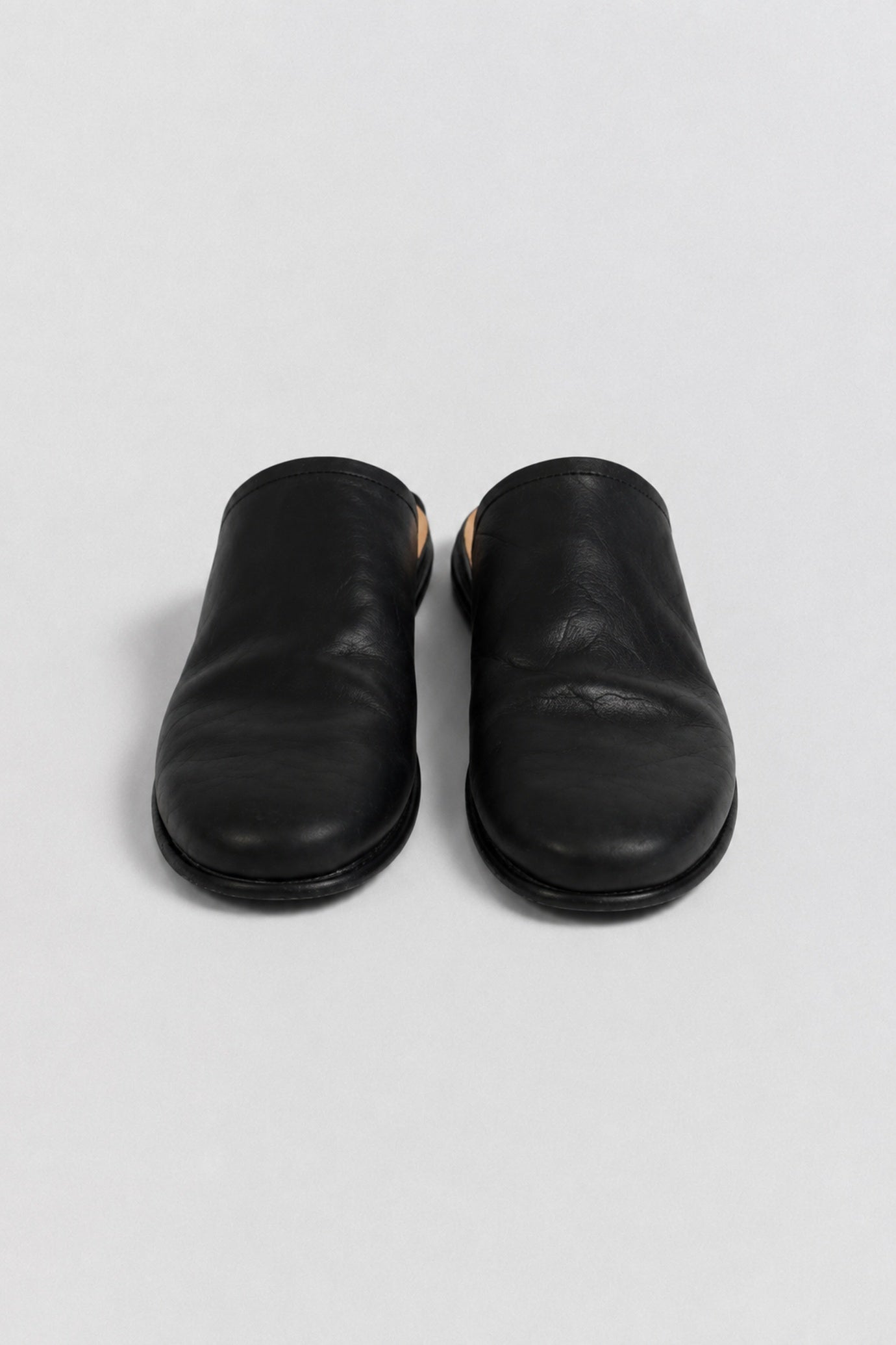 A pair of black leather slip-on clogs with a low round toe, photographed from a top-down angle on a light gray background.