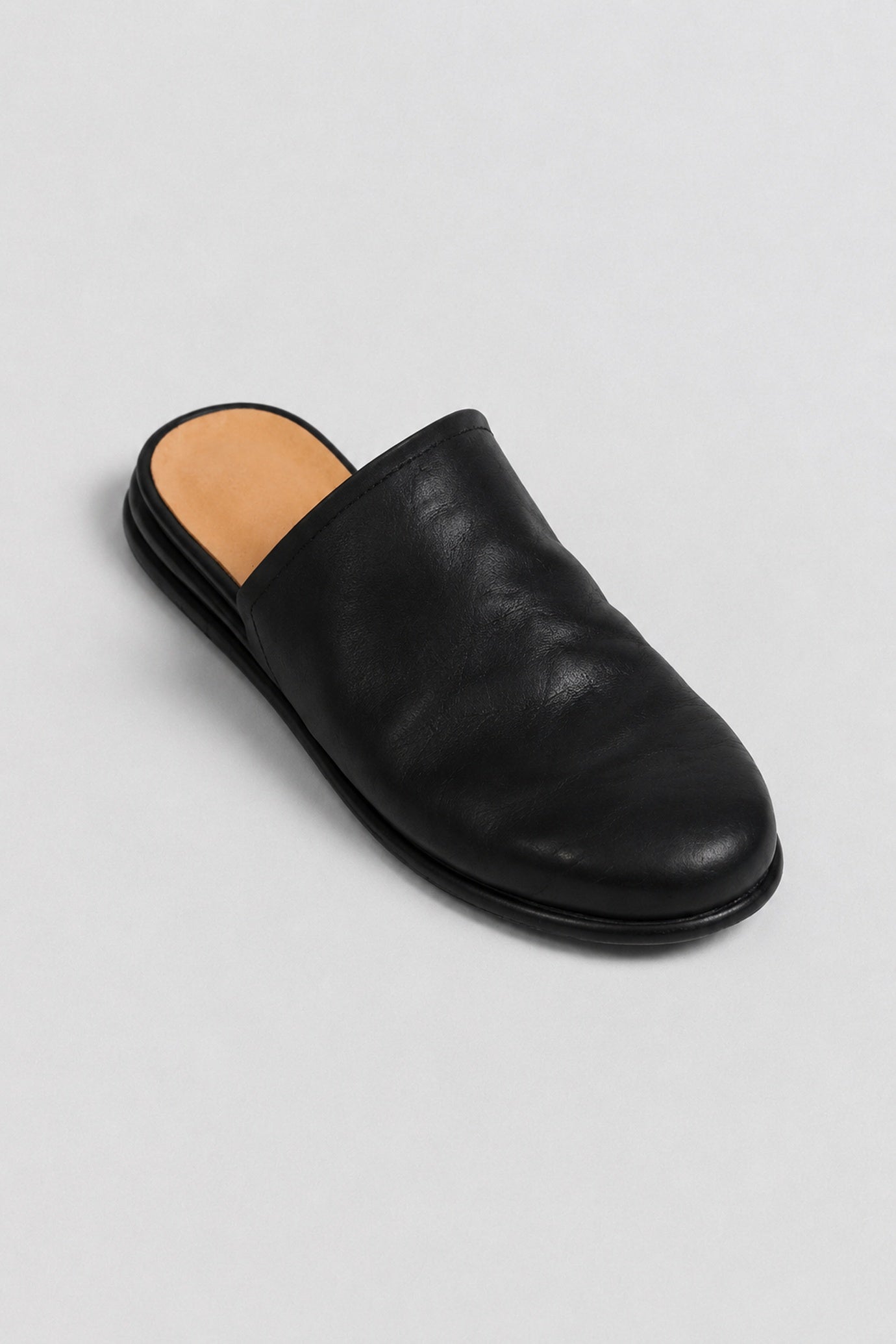 A single black leather mule slipper with a rounded toe and a tan insole, photographed from an elevated angle on a light gray background.