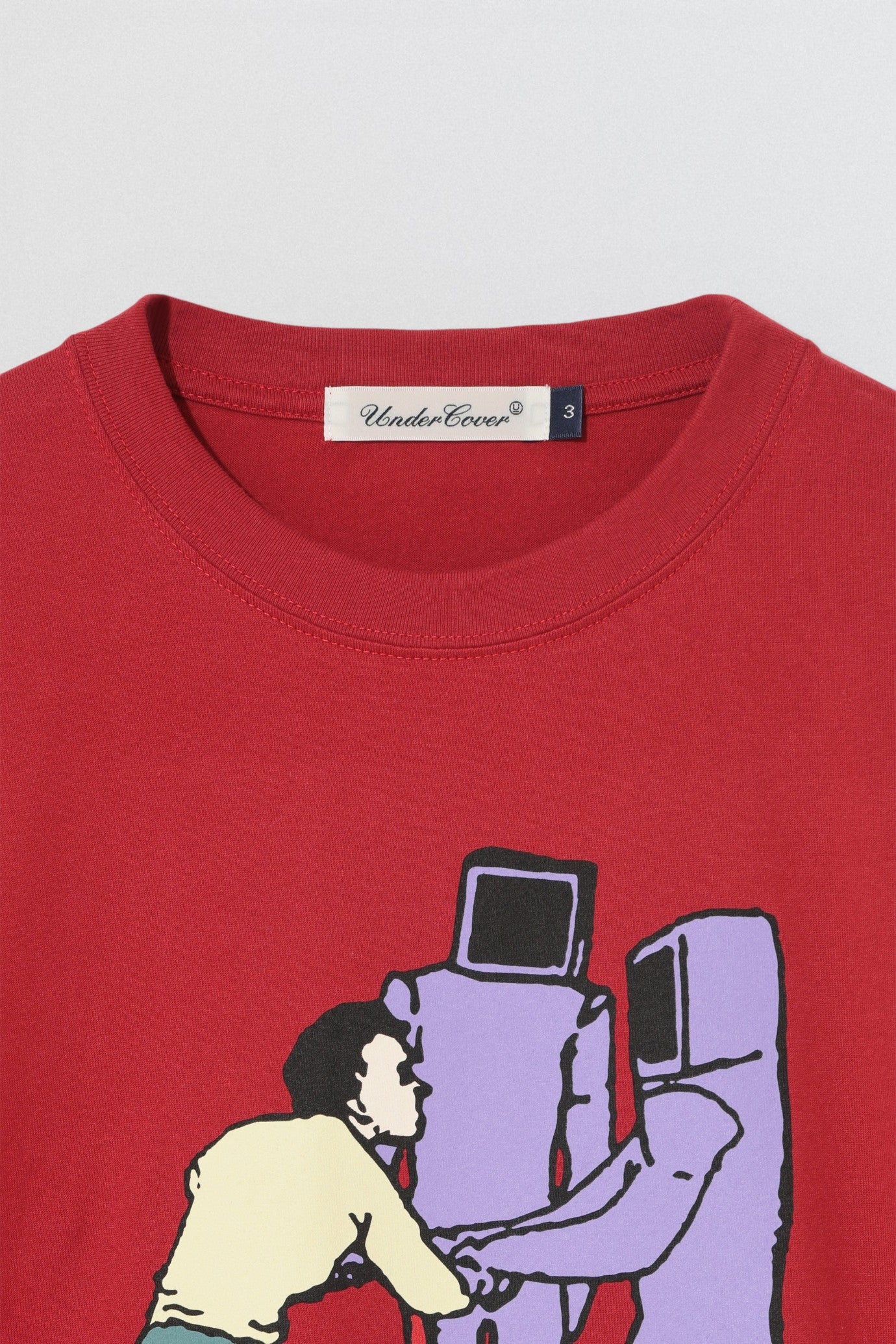Undercover SS26 Bike Man Red t-shirt with graphic design of a person and robot, brand 'Undercover' visible.