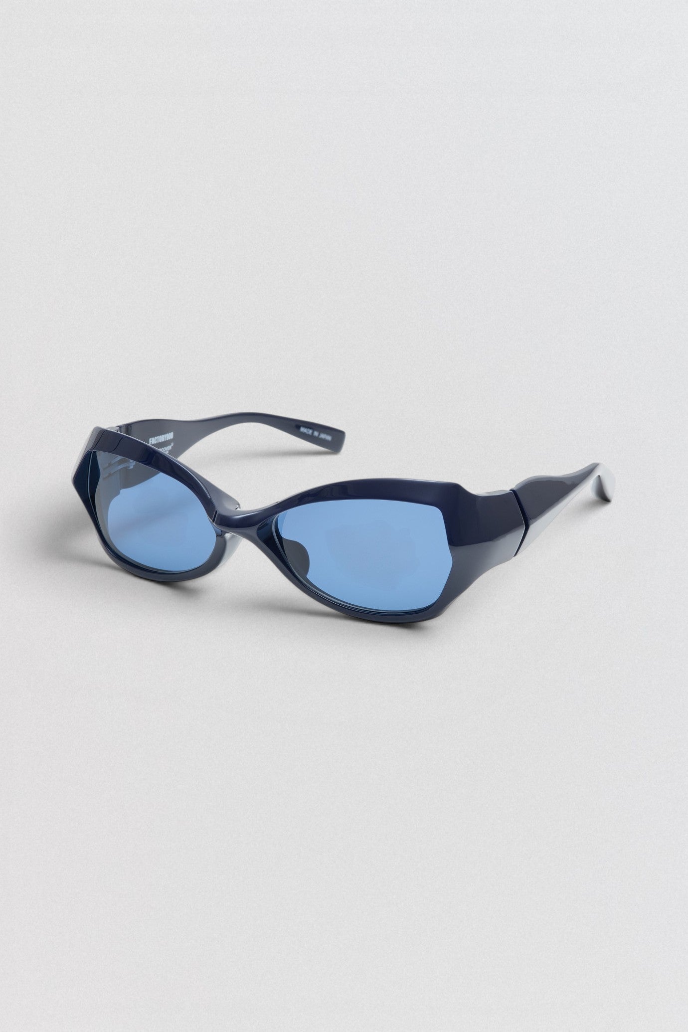 Undercover SS26 Factory900 Blue sunglasses with a cat-eye design on a light gray background