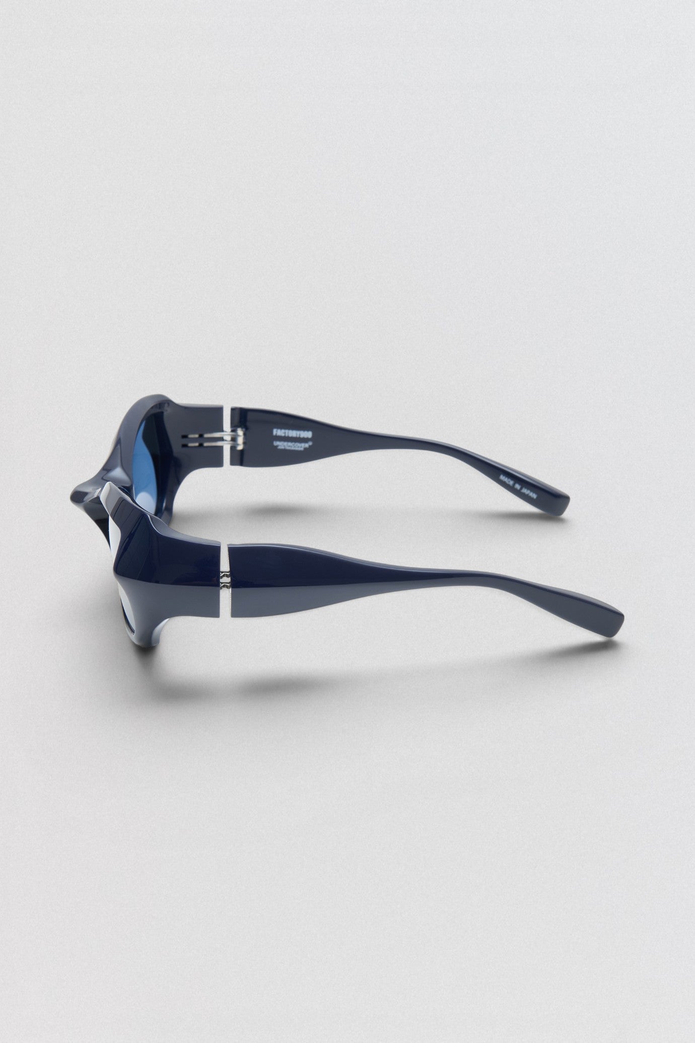 Undercover SS26 Factory900  Pair of sunglasses with blue and black frame on a light gray background