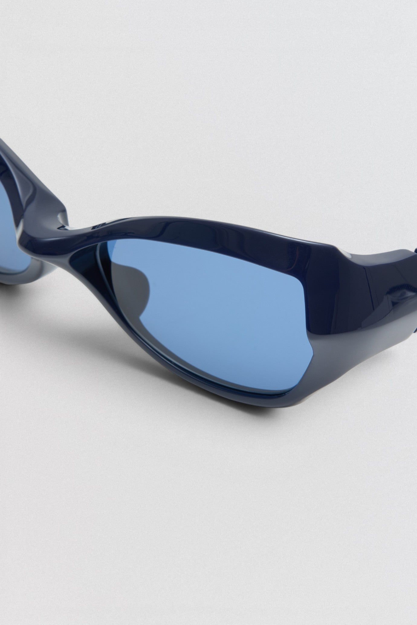 Undercover SS26 Factory900  Blue sunglasses with a reflective lens on a light gray background