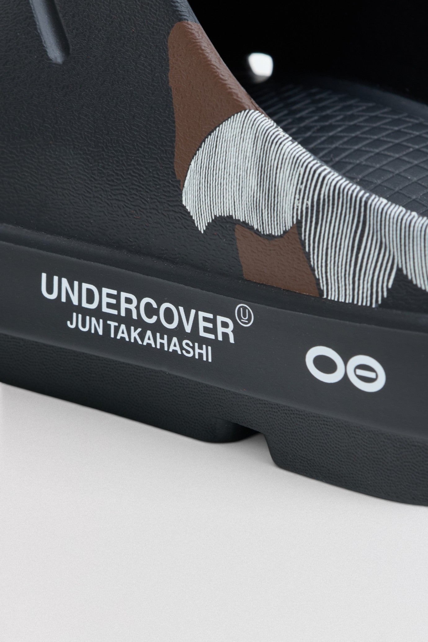 Undercover x OOFOS  Close-up of a sneaker with 'Undercover' branding on a white background