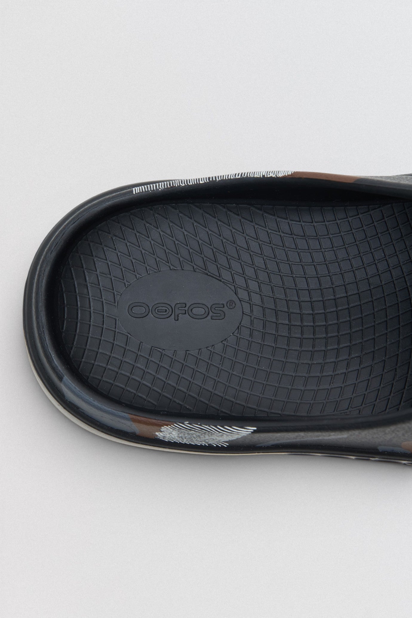 Undercover x OOFOS  Close-up of a black sandal sole with 'Oofos' branding on a light gray background